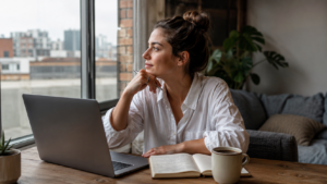 Young adult staying home with a laptop and notebook by a window